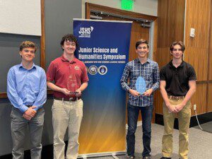 ORHS Students pose with trophies in front of the Junior Science and Humanities Symposium banner after winning first and third in the competition